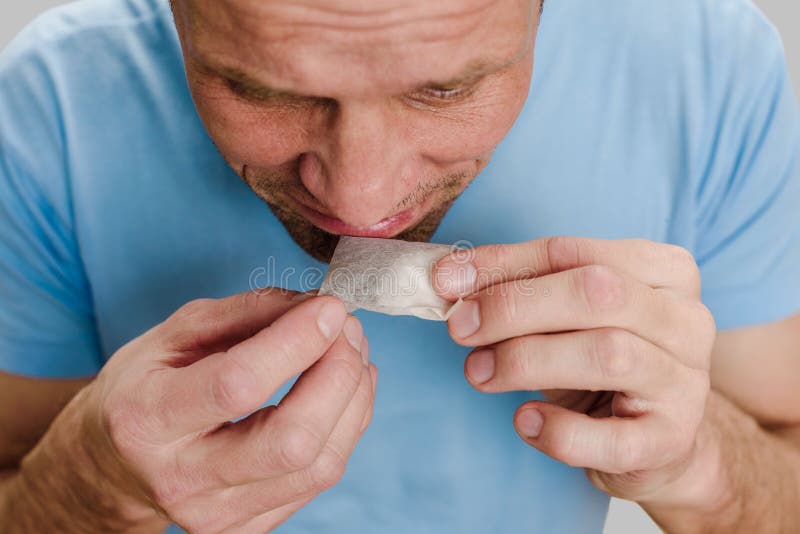 Closeup photo of man with flu infection suffering from anosmia trying to smell teabag. Fragrant reminiscence: Man reflects on loss, stirred by a smell. Closeup photo of man with flu infection suffering from anosmia trying to smell teabag. Fragrant reminiscence: Man reflects on loss, stirred by a smell
