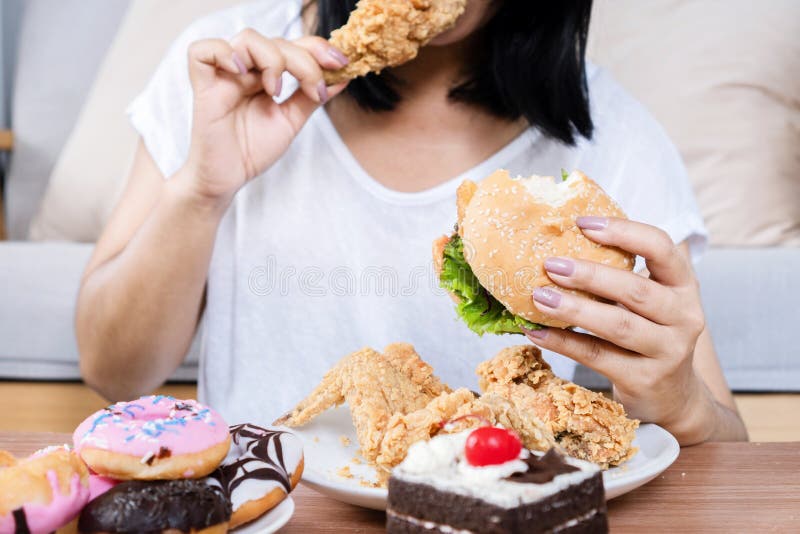 Binge eating disorder concept with woman eating fast food burger, fired chicken , donuts and desserts, eating too much. Binge eating disorder concept with woman eating fast food burger, fired chicken , donuts and desserts, eating too much