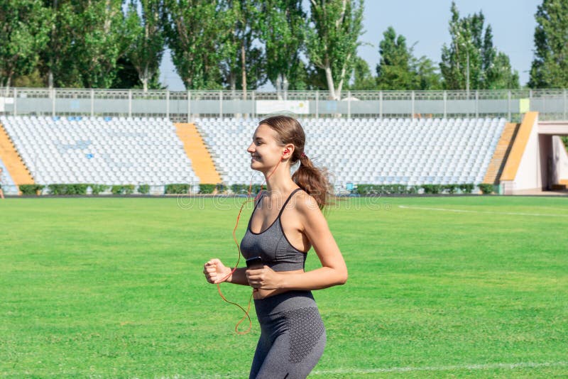 Konditionkvinna i lyssnande musik och spring för sportswear på fotbollsarenan Sportar och sunt begrepp royaltyfri foto Konditionkvinna i lyssnande musik och spring för sportswear på fotbollsarenan Sportar och sunt begrepp royaltyfri foto