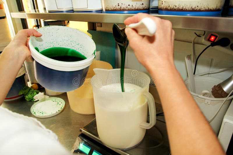 Konditor i kocklikformig tillfogar mintkaramellextrakt med spateln Kvinnan tillfogar en mintkaramellextrakt och en koncentrat til royaltyfri fotografi Konditor i kocklikformig tillfogar mintkaramellextrakt med spateln Kvinnan tillfogar en mintkaramellextrakt och en koncentrat til royaltyfri fotografi