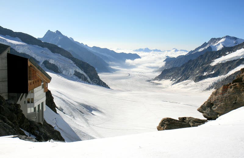 The Konkordiaplatz (2799 m) and the mountain ridges of the high snow-covered peaks of the Alps in the middle of Switzerland, seen from the Jungfraujoch. The Konkordiaplatz is the highest part of the 23.5 kilometers long Aletsch Glacier. From the Kleine Scheidegg, the Jungfrau Railway begins a remarkable journey through the Eiger to the Jungfraujoch - Top of Europe. This remarkable round-trip by modern cogwheel railway is one of European top holiday attractions. On the left a little part of the Sphinx Observatory. The Konkordiaplatz (2799 m) and the mountain ridges of the high snow-covered peaks of the Alps in the middle of Switzerland, seen from the Jungfraujoch. The Konkordiaplatz is the highest part of the 23.5 kilometers long Aletsch Glacier. From the Kleine Scheidegg, the Jungfrau Railway begins a remarkable journey through the Eiger to the Jungfraujoch - Top of Europe. This remarkable round-trip by modern cogwheel railway is one of European top holiday attractions. On the left a little part of the Sphinx Observatory.