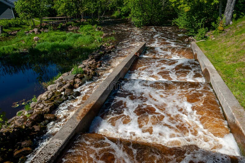 Konstgjord vattenfallskrascade under vattentrappan på en flodkanal i Zaslavl belarus. ljust gröngräs och blått royaltyfria bilder