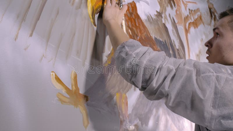 Artist designer draws an eagle on the wall. Craftsman decorator paints a picture with acrylic oil color. Painter painter dressed in a paint coat. Indoor. Dark magic cinematic look. Artist designer draws an eagle on the wall. Craftsman decorator paints a picture with acrylic oil color. Painter painter dressed in a paint coat. Indoor. Dark magic cinematic look.