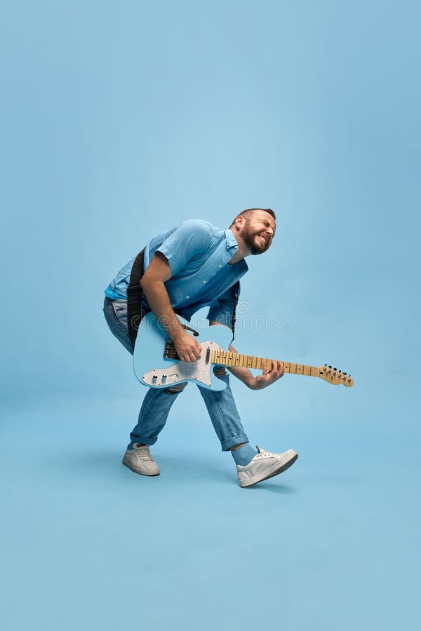 Konstnärlig talangmusiker i tillfälliga kläder som spelar elektrisk gitarr mot blå studiobakgrund arkivfoto