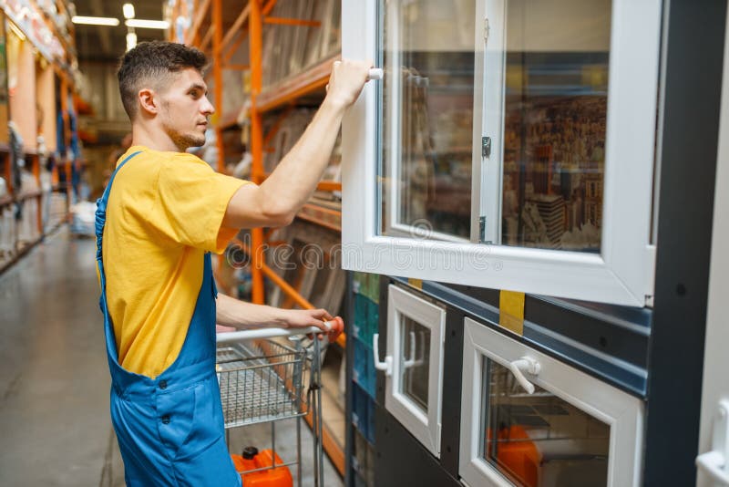 Male constructor choosing windows in hardware store. Builder in uniform look at the goods in diy shop. Male constructor choosing windows in hardware store. Builder in uniform look at the goods in diy shop