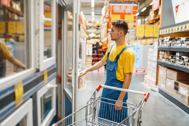 Male constructor choosing windows in hardware store. Builder in uniform look at the goods in diy shop. Male constructor choosing windows in hardware store. Builder in uniform look at the goods in diy shop