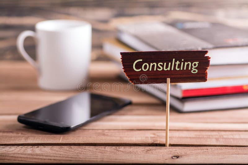 Consulting on wooden sign with book , coffee cup and mobile phone on wooden table. Consulting on wooden sign with book , coffee cup and mobile phone on wooden table