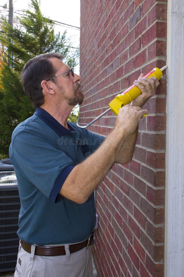 Contractor caulking exterior walls between frame and brick, sealing to stop possible air leaks, conserving energy. Contractor caulking exterior walls between frame and brick, sealing to stop possible air leaks, conserving energy