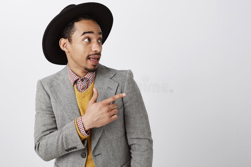 Kontrollera detta ut, mannen Stående av den stiliga fascinerade mörkhyade mannen i stilfull hatt och flott dräkt som pekar och arkivfoto Kontrollera detta ut, mannen Stående av den stiliga fascinerade mörkhyade mannen i stilfull hatt och flott dräkt som pekar och arkivfoto