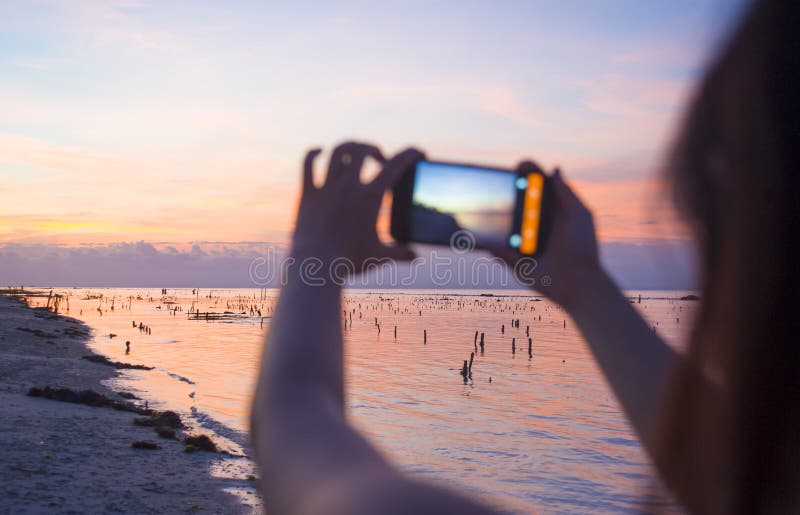 Kontur av den unga kvinnan med mobiltelefonkameran som tar bilden av den härliga Agung för för strandsolnedgånglandskap och monte fotografering för bildbyråer