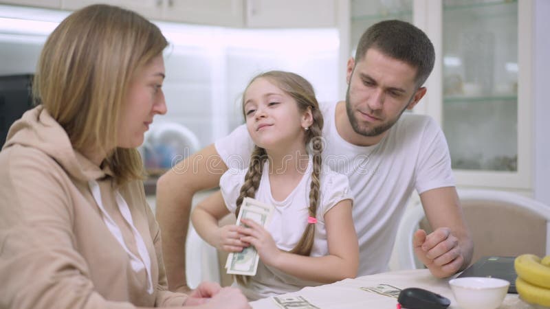 Konzentriertes kleines Mädchen, das Dollar zählt und Geld mit Vater und Mutter teilt. Porträt von fröhlich niedlich kaukasisch stock footage