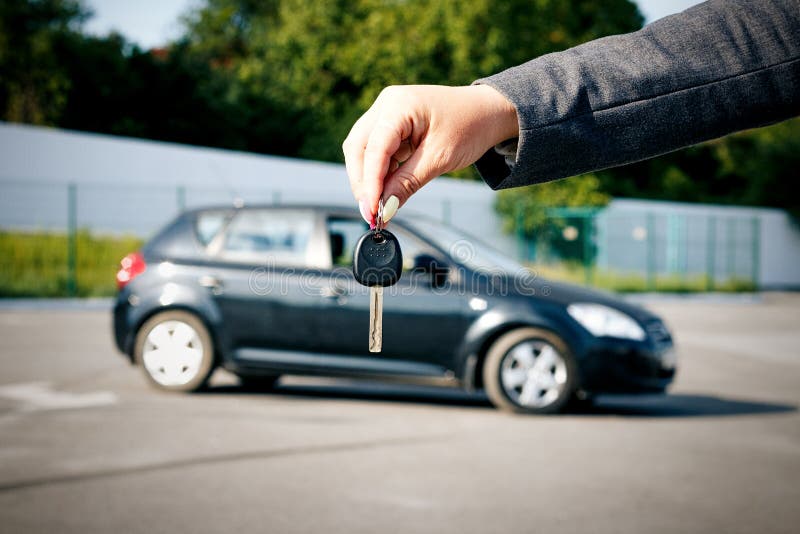 Concept of buying, selling and renting a car. A female hand holds the car key against the background of the car. With a place for advertising text. Concept of buying, selling and renting a car. A female hand holds the car key against the background of the car. With a place for advertising text.