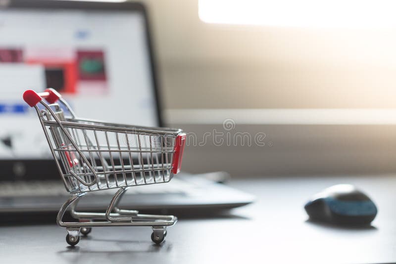 Konzept des on-line-Einkaufens: Wenig Einkaufswagen und ein Laptop im undeutlichen Hintergrund