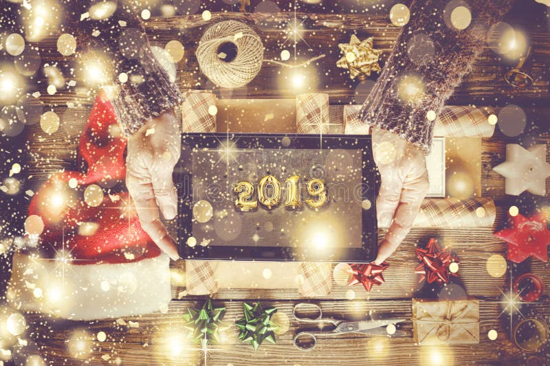 2019. Concept New Year, golden snowflakes. In the hands of a woman Tablet PC with a picture of 2019 on the background of a table with items for New Year`s gifts. 2019. Concept New Year, golden snowflakes. In the hands of a woman Tablet PC with a picture of 2019 on the background of a table with items for New Year`s gifts.