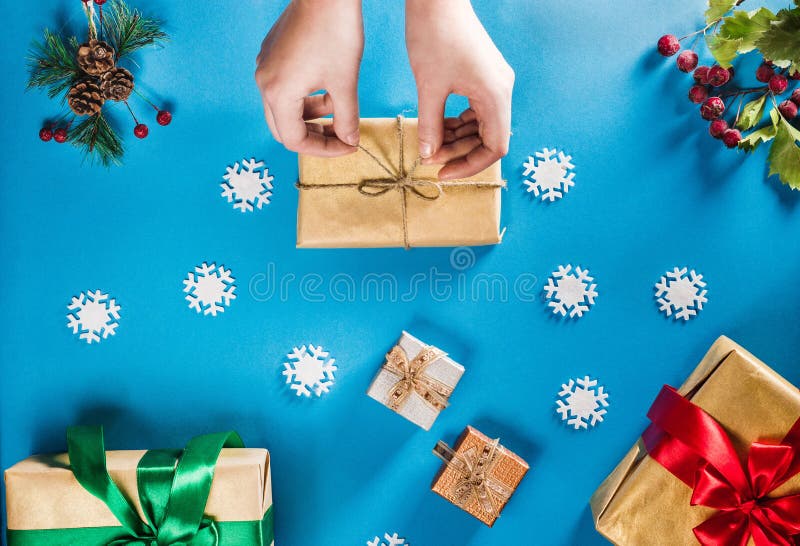 Concept of Christmas items on a bright blue background. Woman`s hands wrapping Christmas gift. Flat lay of Christmas decorations, snowflakes, berries and twigs with presents. Concept of Christmas items on a bright blue background. Woman`s hands wrapping Christmas gift. Flat lay of Christmas decorations, snowflakes, berries and twigs with presents