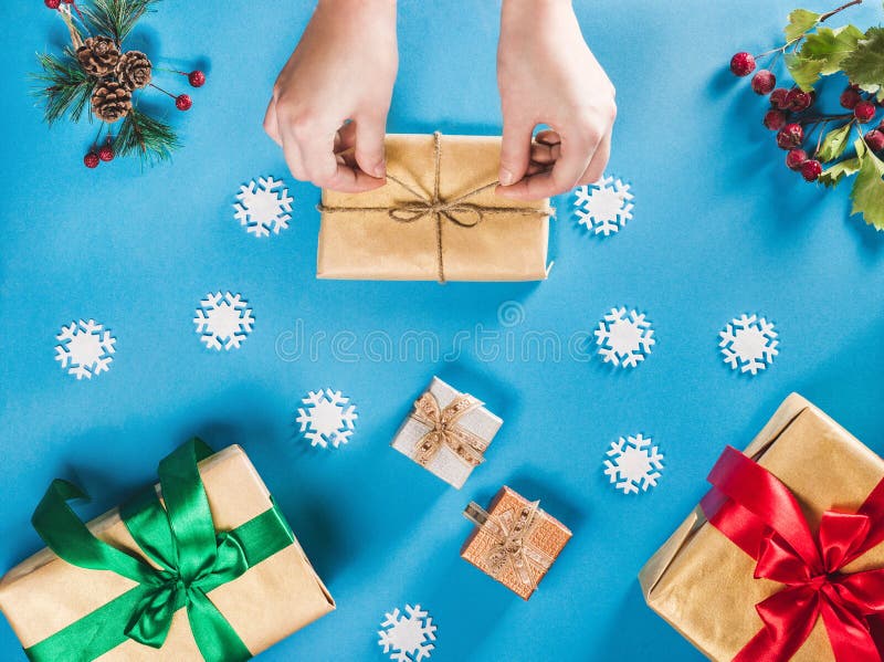 Concept of Christmas items on a bright blue background. Woman`s hands wrapping Christmas gift. Flat lay of Christmas decorations, snowflakes, berries and twigs with presents. Concept of Christmas items on a bright blue background. Woman`s hands wrapping Christmas gift. Flat lay of Christmas decorations, snowflakes, berries and twigs with presents