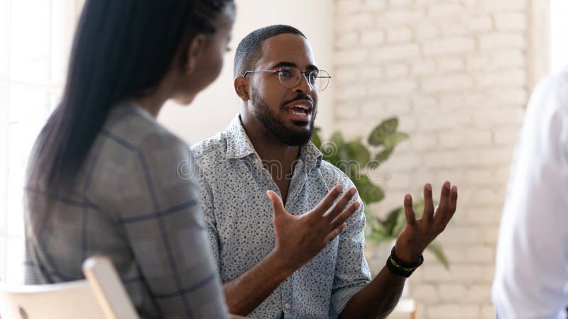 Head shot young african american male psychologist meeting patients at group therapy. Serious mixed race counselor giving advices to employees. Confident business coach training staff at office. Head shot young african american male psychologist meeting patients at group therapy. Serious mixed race counselor giving advices to employees. Confident business coach training staff at office.