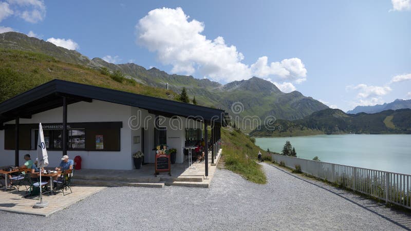 Kopfsseestuberl snack kiosk situated at mountain dam Kops in Silvretta Verwallgruppe mountains - Austria. Fluhspitze and Fadnerspitze mountains in the background. Kopfsseestuberl snack kiosk situated at mountain dam Kops in Silvretta Verwallgruppe mountains - Austria. Fluhspitze and Fadnerspitze mountains in the background.