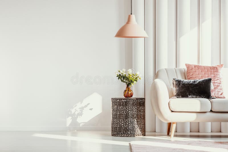 Kopiuj miejsce na białej ścianie eleganckiego salonu z białymi kwiatami na szklanej wazonie na stylowym stole obok białej sofy