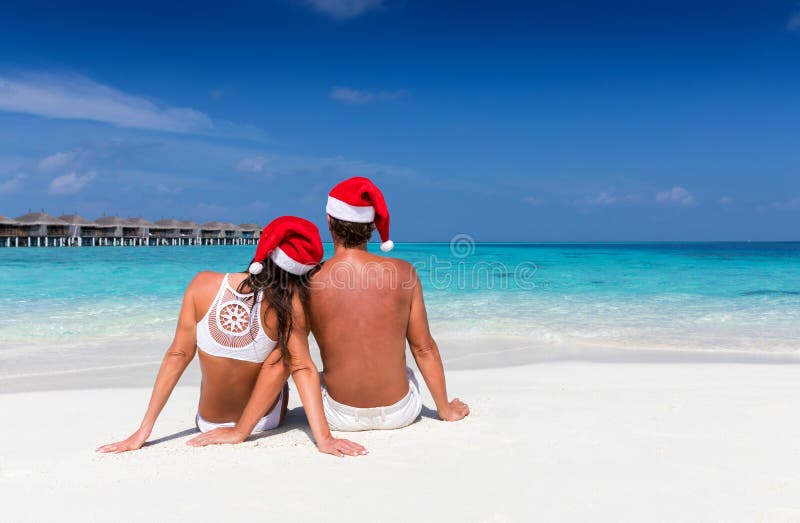 Koppla ihop med julhattar som sitter på en tropisk strand royaltyfri bild Koppla ihop med julhattar som sitter på en tropisk strand royaltyfri bild