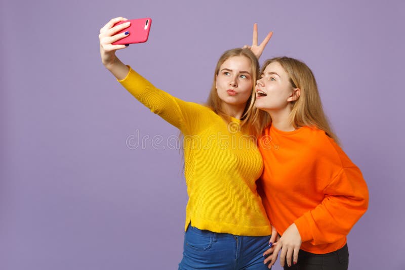 Kopplar samman gladlynt ung blondin två systerflickor i färgrik kläder som gör selfie som skjutas på mobiltelefonen som isoleras royaltyfri fotografi Kopplar samman gladlynt ung blondin två systerflickor i färgrik kläder som gör selfie som skjutas på mobiltelefonen som isoleras royaltyfri fotografi