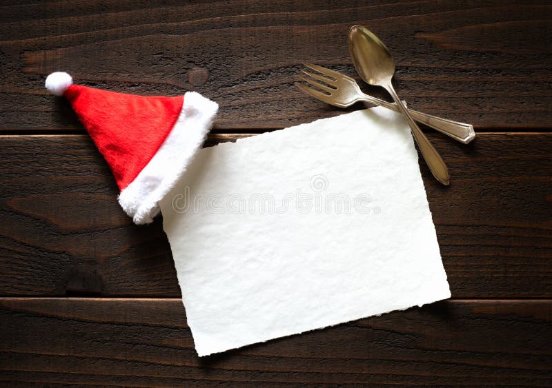 Kort för julferiepapper med den röda och vita Santa Claus Hat och gaffeln och sked på mörk lantlig trätabellbakgrund