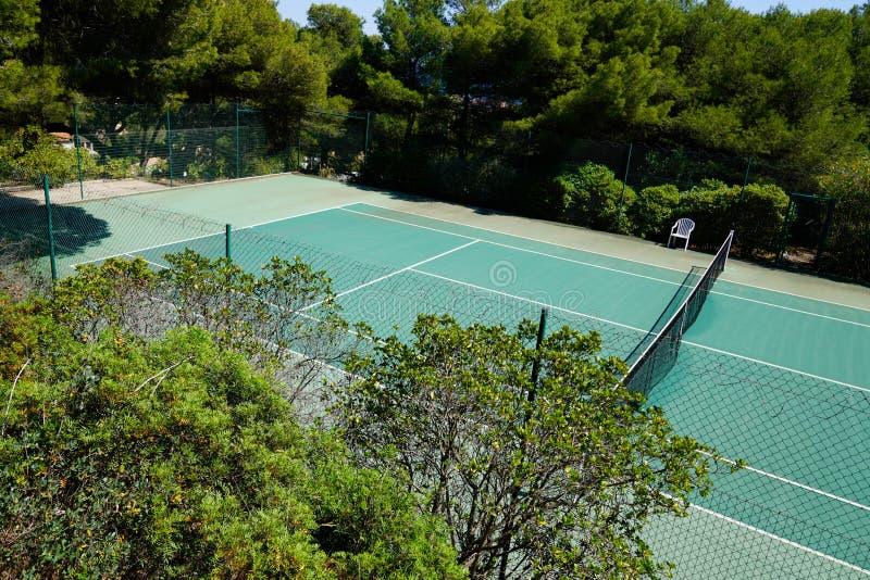 A tennis courts green private house through wire mesh fence in home garden. A tennis courts green private house through wire mesh fence in home garden