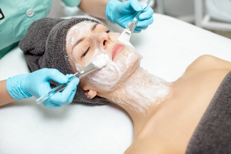 Kosmetiker wendet Gesichtsmaske auf schöner junger Frau im Badekurortsalon an kosmetische Verfahrenshautpflege Microdermabrasion stockbild Kosmetiker wendet Gesichtsmaske auf schöner junger Frau im Badekurortsalon an kosmetische Verfahrenshautpflege Microdermabrasion stockbild