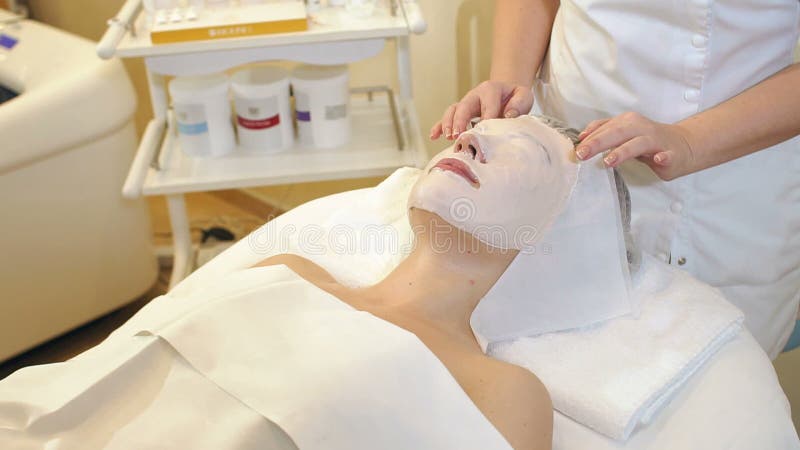 Kosmetologen tar bort en leramaskering fr?n framsidan av en ung flicka i den Spa salongen