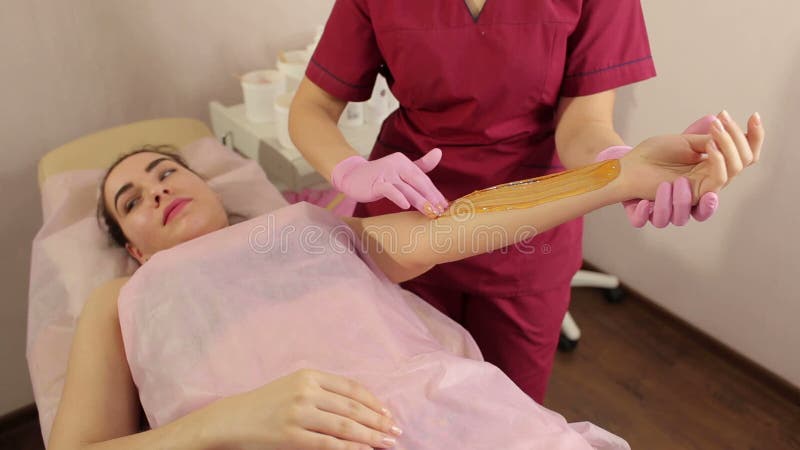 Kosmetologen tar bort hår från en kvinnas hand sockra