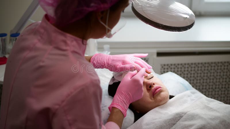 Kosmetologen tar bort målarfärgrest med lokalvårdtorkduken från ögonbrynflicka