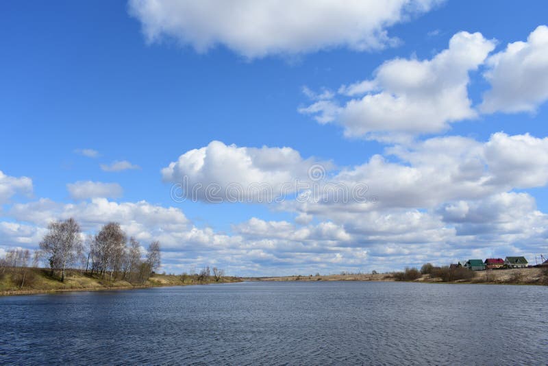 The Kostroma River. On the high banks are village houses, trees and green grass. There are white clouds in the blue sky. Wind royalty free stock photography