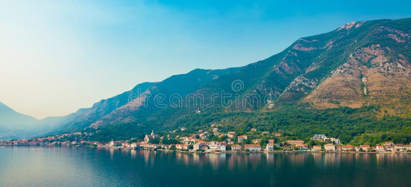 Idyllic view of the fjords in Kotor. Town with red roofed houses along the waterfront, mountains and blue sky. Bay of Kotor, Montenegro, Europe. Idyllic view of the fjords in Kotor. Town with red roofed houses along the waterfront, mountains and blue sky. Bay of Kotor, Montenegro, Europe