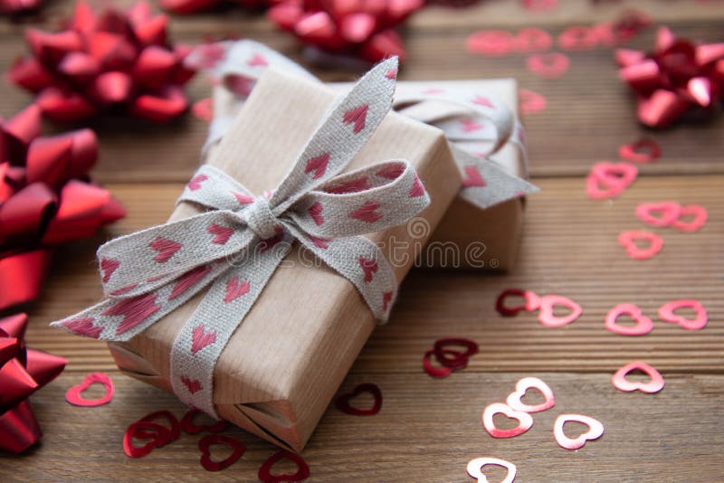 Kraft brown paper gift box with red bows and confetti, on wooden background. Valentine& x27;s Day, Birthday, Party concept