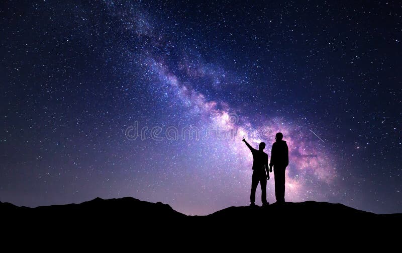 Milky Way with silhouette of a family on the mountain. Father and a son who pointing finger in night starry sky. Night landscape. Beautiful Universe. Space. Travel background with sky full of stars. Milky Way with silhouette of a family on the mountain. Father and a son who pointing finger in night starry sky. Night landscape. Beautiful Universe. Space. Travel background with sky full of stars