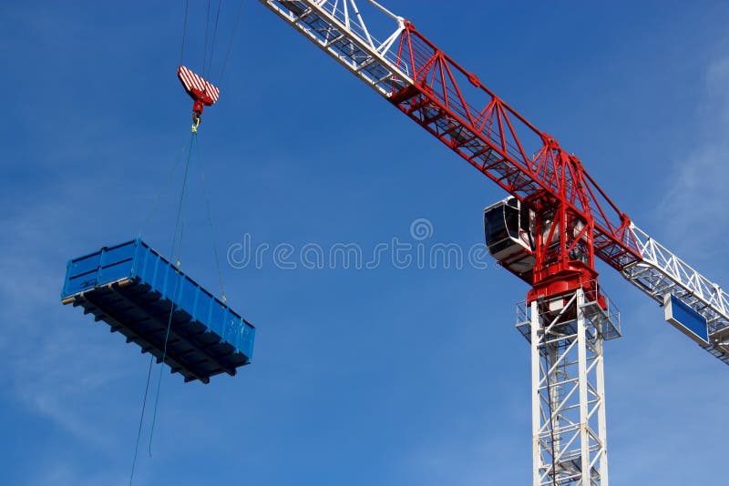 Construction site crane is lifting truck dumpster on the blue sky. Construction site crane is lifting truck dumpster on the blue sky