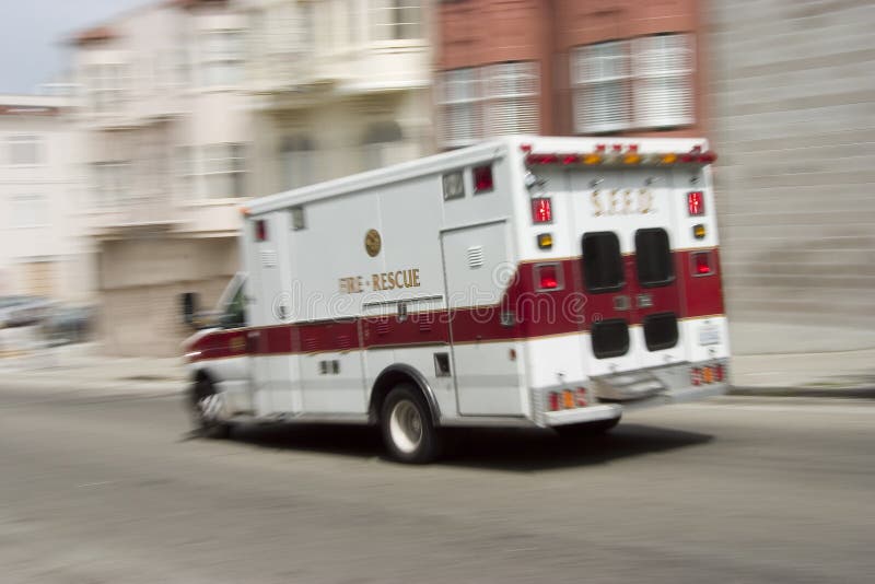 An ambulance blazes by, it's sirens whaling. An intensional camera blur gives a feeling of a rushed tension to the scene. An ambulance blazes by, it's sirens whaling. An intensional camera blur gives a feeling of a rushed tension to the scene.