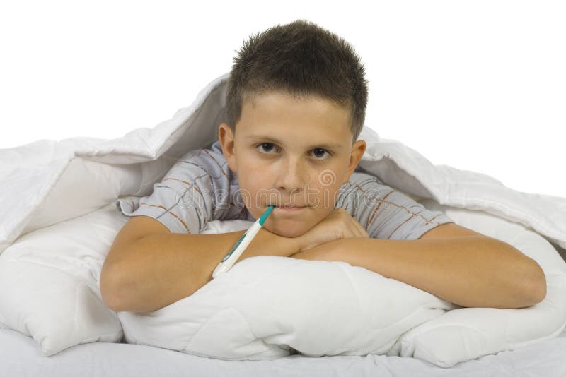 Young boy lying on bed with thermometer in mouth. Looking at camera. White background. Young boy lying on bed with thermometer in mouth. Looking at camera. White background