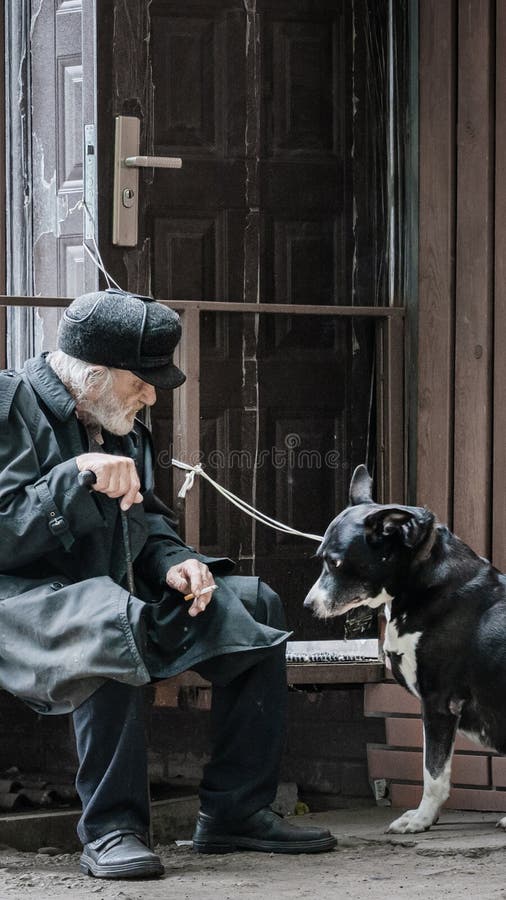 Krasnoyarsk Ryssland, 24 juli, 2019: en enslig farfar med hans hund sitter ledset och röker cigaretten Mjuk fokus, suddighet royaltyfri bild Krasnoyarsk Ryssland, 24 juli, 2019: en enslig farfar med hans hund sitter ledset och röker cigaretten Mjuk fokus, suddighet royaltyfri bild