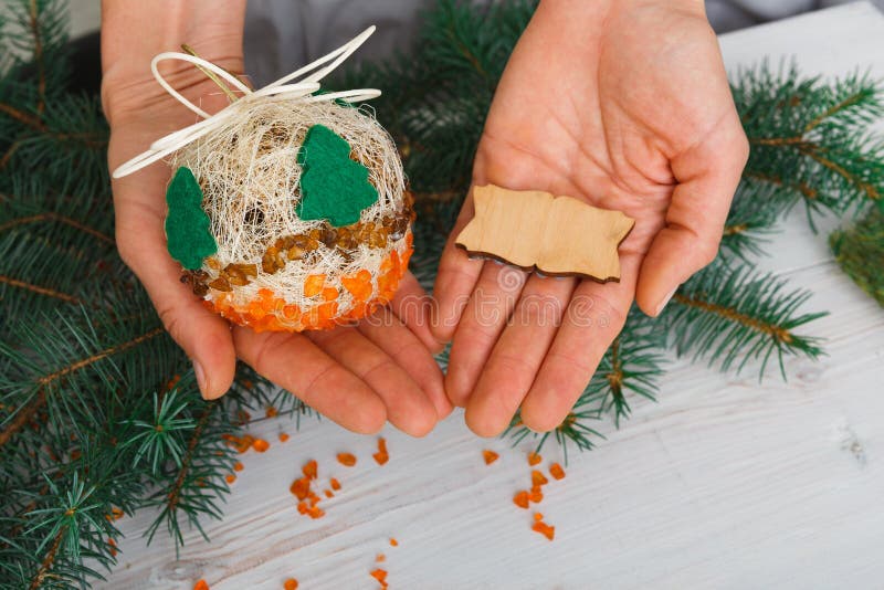 Creative diy craft hobby. Woman shows craft christmas ball with felt spruce tree and empty wooden lable with copy space. Home leisure, holiday decorations. Closeup of female hands at wood background. Creative diy craft hobby. Woman shows craft christmas ball with felt spruce tree and empty wooden lable with copy space. Home leisure, holiday decorations. Closeup of female hands at wood background