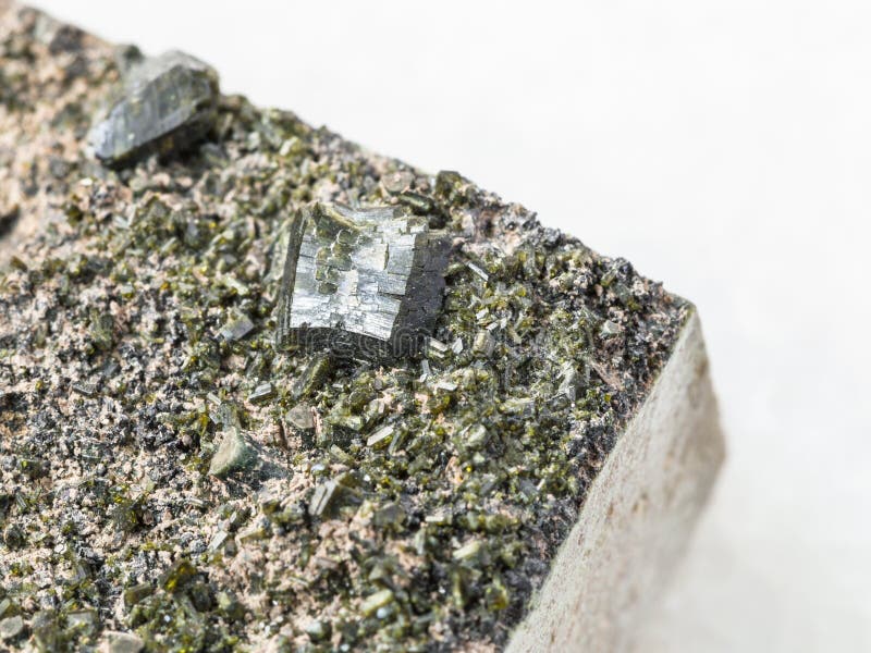 Kristaller av Epidote på stenslut upp på vit. Makroskytte av det naturliga mineraliska stenprovet - kristaller av Epidoteslutet upp på stenen på vit marmorbakgrund från den Irkutsk regionen, Ryssland