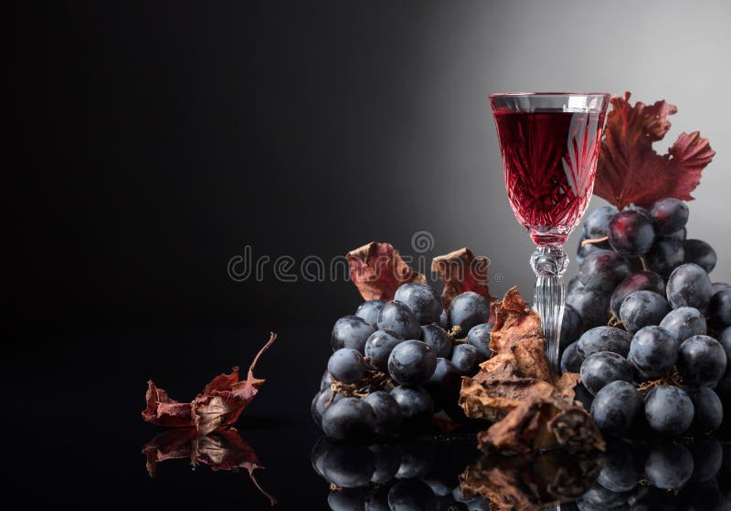 Kristallglas Rotwein und Trauben mit getrockneten Weinblättern lizenzfreie stockbilder Kristallglas Rotwein und Trauben mit getrockneten Weinblättern lizenzfreie stockbilder
