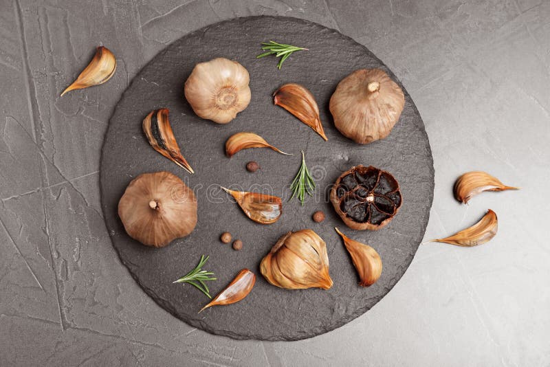 Slate plate with aged black garlic and rosemary on gray background, top view. Slate plate with aged black garlic and rosemary on gray background, top view