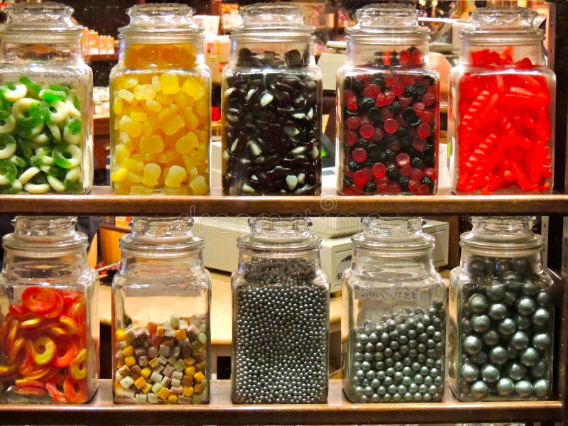 Racks of jars seen through the shop window of a candy store with silver bearings, cough candies, dolly mixture, sours, and red and black gums with other sweets. Racks of jars seen through the shop window of a candy store with silver bearings, cough candies, dolly mixture, sours, and red and black gums with other sweets