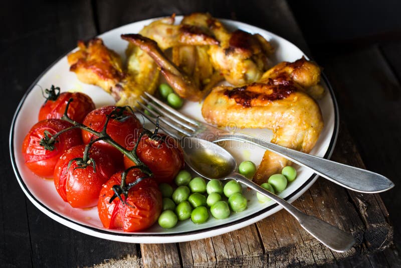 Kryddiga fega vingar, grillade körsbärsröda tomater och gröna ärtor Baslanced mål royaltyfri bild Kryddiga fega vingar, grillade körsbärsröda tomater och gröna ärtor Baslanced mål royaltyfri bild