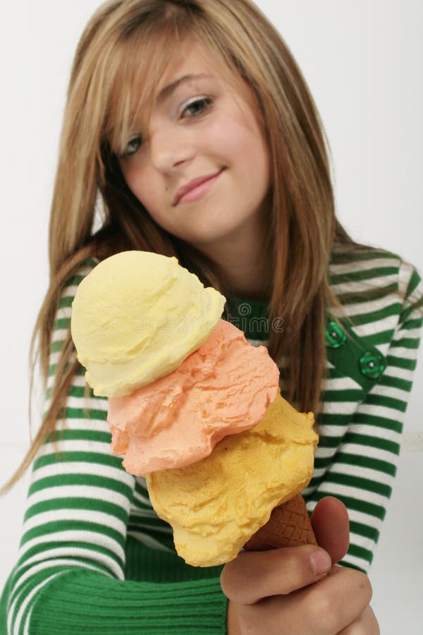 A young girl smiles and holds out an ice-cream cone with three scoops of ice-cream as if asking if you want some too. A young girl smiles and holds out an ice-cream cone with three scoops of ice-cream as if asking if you want some too.