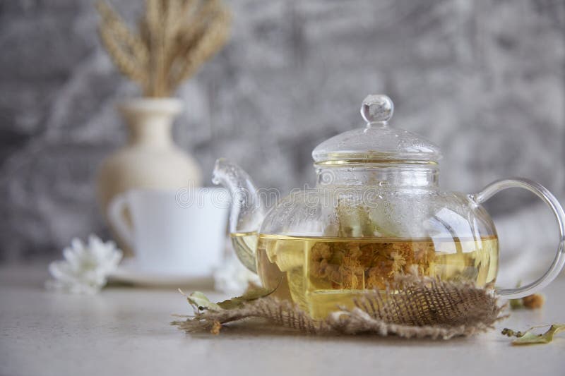 Kräuterleinentee in Teekanne mit Tasse Tee. Relaxzeit. umweltverträgliche nachhaltige Lebensweise. Weizenchrysanthemen stockbilder