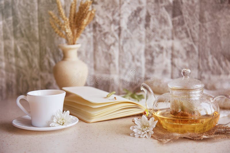 Kräuterleinentee in Teekanne mit Tasse Tee. Weizenblumen Herbstdekorationen und Notizbuch. gemütliche Atmosphäre entspannen stockfotos