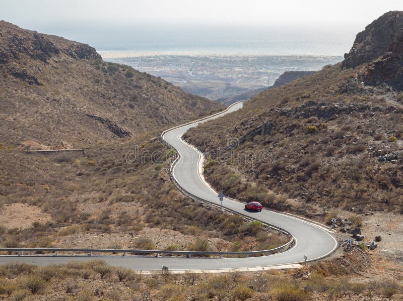 Krökt slingrig väg med en röd bil i bergen i Gran Canaria royaltyfri foto Krökt slingrig väg med en röd bil i bergen i Gran Canaria royaltyfri foto
