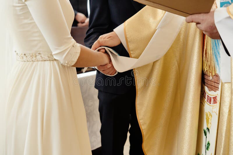 Ksiądz trzymający w rękach stylową pannę młodą i eleganckiego pana młodego na ceremonii ślubnej w kościele